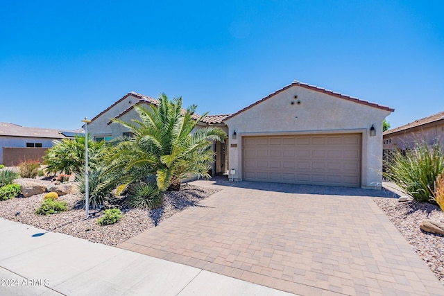 view of front of property with decorative driveway, an attached garage, a tile roof, and stucco siding