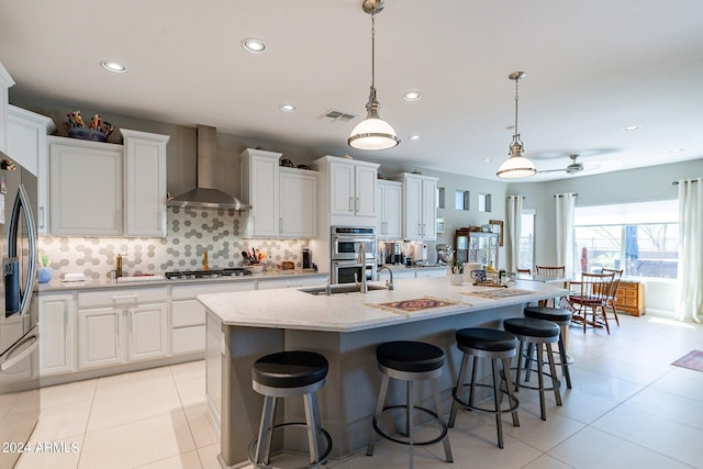 kitchen with pendant lighting, white cabinetry, wall chimney exhaust hood, and a center island with sink