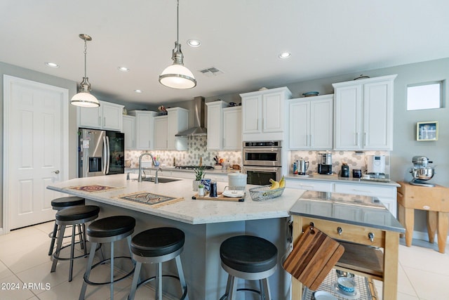 kitchen featuring sink, appliances with stainless steel finishes, wall chimney range hood, a kitchen island with sink, and white cabinets