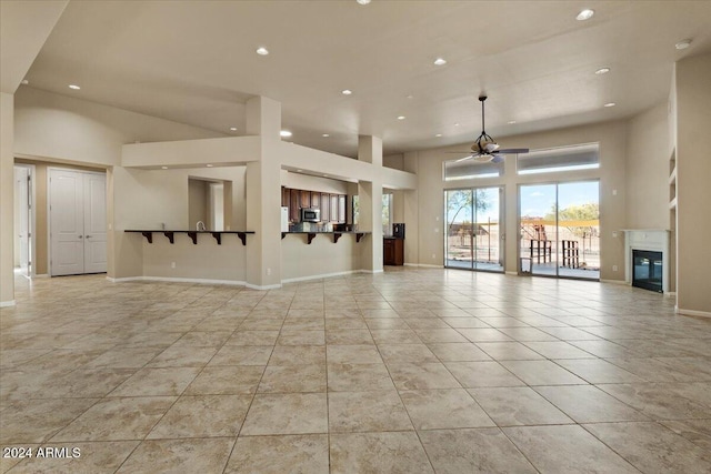 unfurnished living room with ceiling fan, light tile patterned flooring, and a towering ceiling