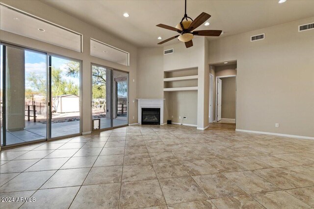 unfurnished living room featuring ceiling fan, built in features, and a towering ceiling