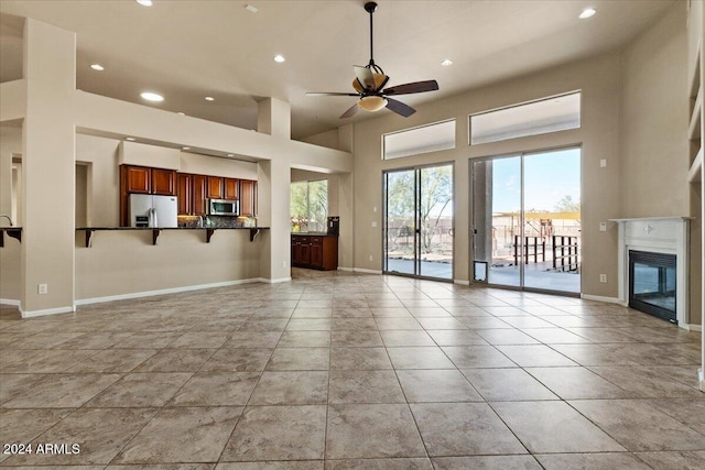 unfurnished living room featuring a high ceiling, light tile patterned floors, and ceiling fan