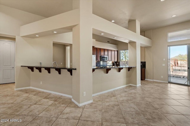 kitchen featuring kitchen peninsula, sink, light tile patterned floors, white fridge, and a breakfast bar area