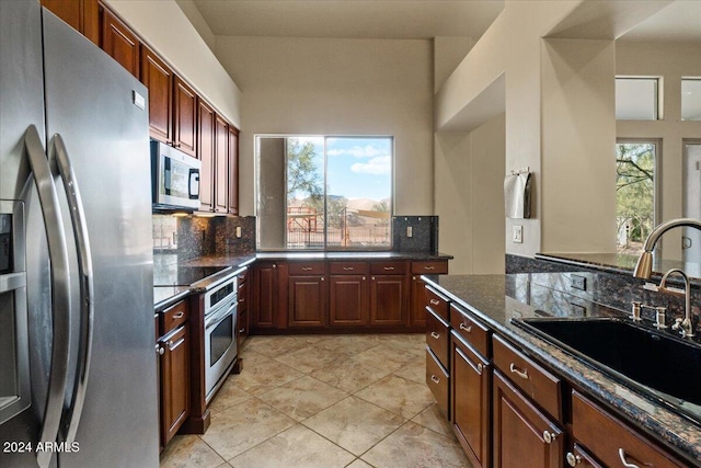 kitchen featuring sink, stainless steel appliances, tasteful backsplash, dark stone counters, and light tile patterned floors