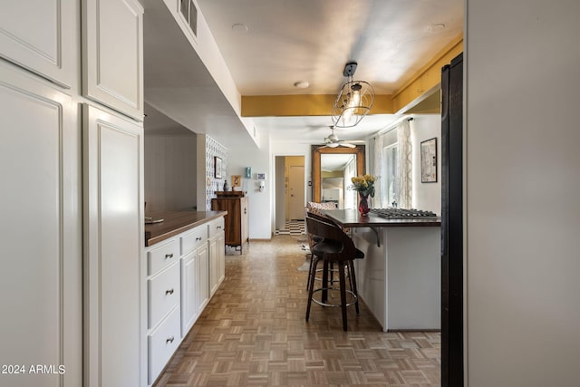 kitchen with a kitchen bar, wooden counters, white cabinetry, and dark parquet floors