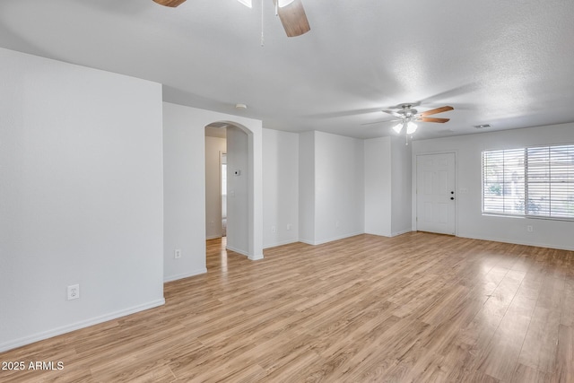 spare room with visible vents, ceiling fan, baseboards, light wood-style floors, and arched walkways