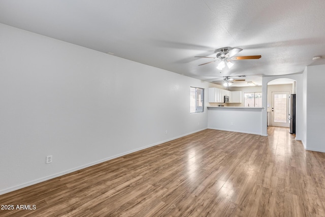 unfurnished living room with light wood-type flooring, arched walkways, baseboards, and a ceiling fan