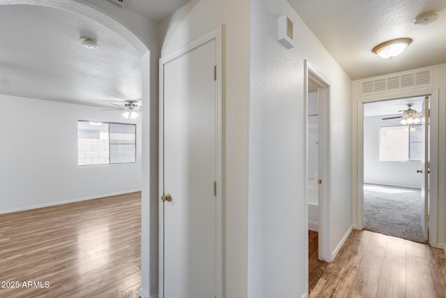 corridor with baseboards, arched walkways, light wood finished floors, and a textured ceiling