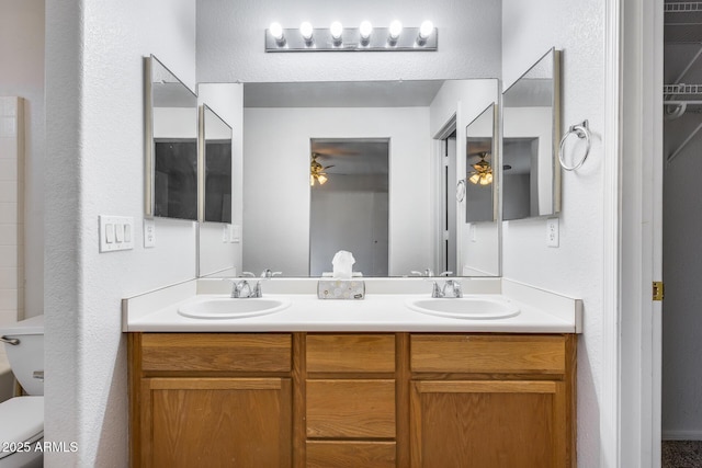 bathroom with double vanity, toilet, a ceiling fan, and a sink