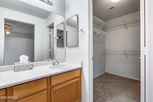 bathroom with a walk in closet, visible vents, baseboards, ceiling fan, and vanity