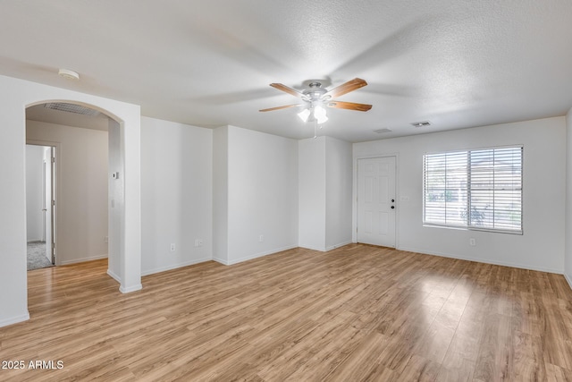 empty room featuring baseboards, ceiling fan, light wood-style flooring, arched walkways, and a textured ceiling