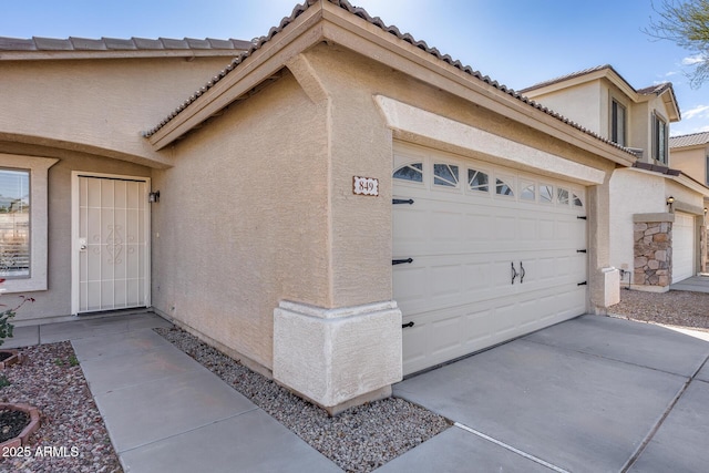 view of side of property with a garage, a tile roof, concrete driveway, and stucco siding