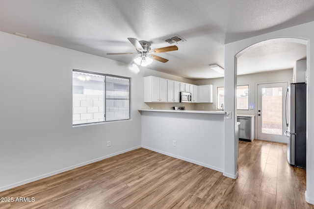 kitchen featuring visible vents, light wood-style flooring, arched walkways, stainless steel appliances, and white cabinets