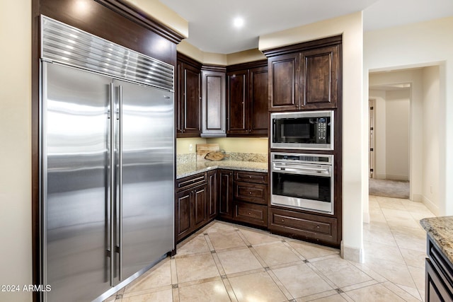 kitchen featuring light stone countertops, dark brown cabinets, and built in appliances