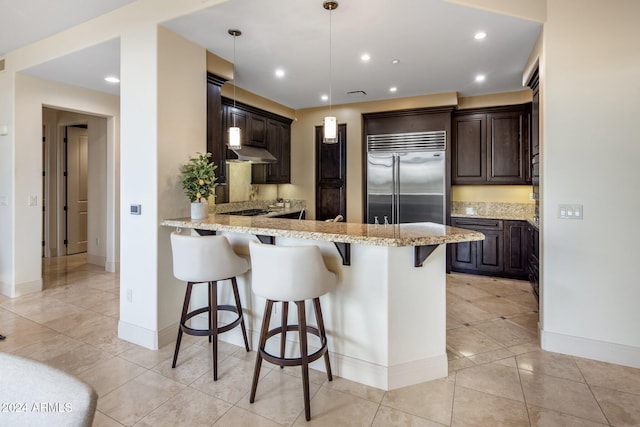 kitchen with built in fridge, dark brown cabinets, a kitchen bar, hanging light fixtures, and kitchen peninsula