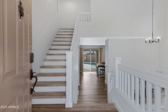 stairs with an inviting chandelier, wood finished floors, and a towering ceiling