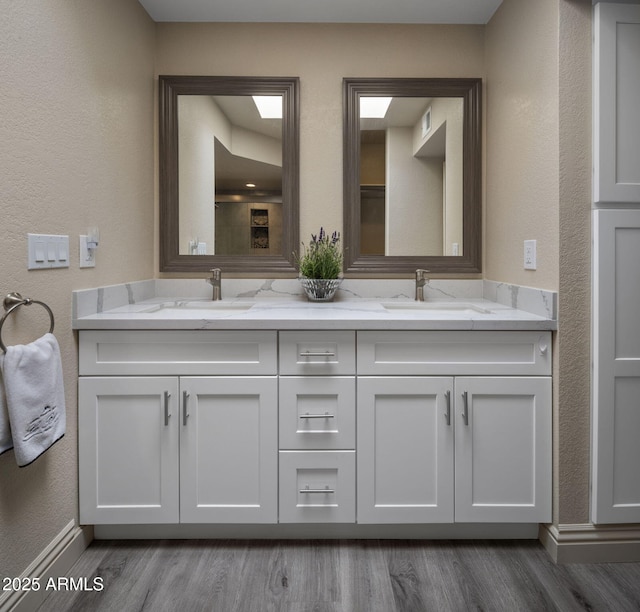 bathroom with wood finished floors, a textured wall, baseboards, and double vanity