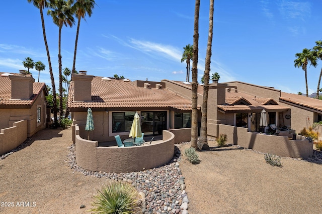 back of house with a tiled roof, a chimney, stucco siding, and a patio area