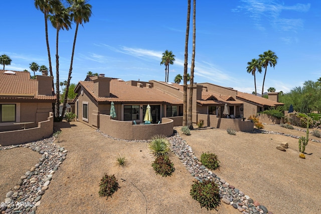 rear view of house featuring a tiled roof, stucco siding, fence, and a chimney