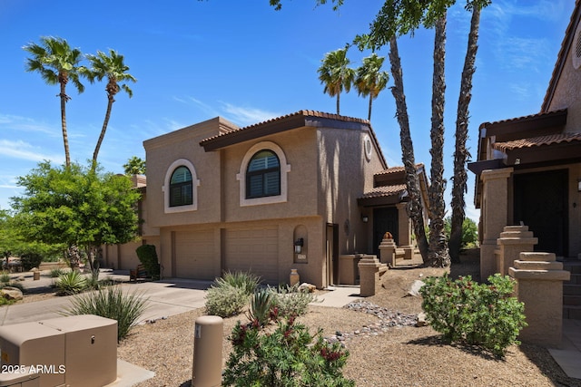 mediterranean / spanish-style home featuring a tile roof, concrete driveway, an attached garage, and stucco siding