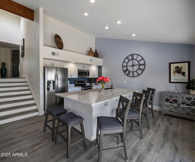 kitchen with appliances with stainless steel finishes, a breakfast bar, baseboards, dark wood-style flooring, and recessed lighting