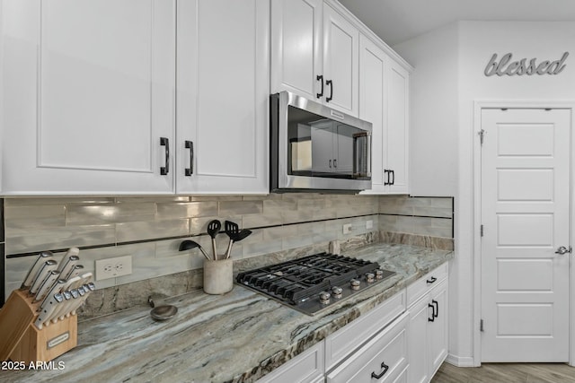 kitchen featuring tasteful backsplash, white cabinetry, stainless steel appliances, and light stone counters