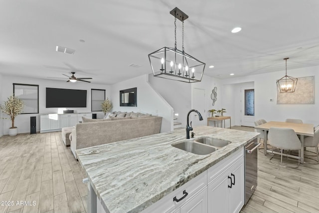 kitchen with light stone counters, a kitchen island with sink, sink, white cabinets, and hanging light fixtures