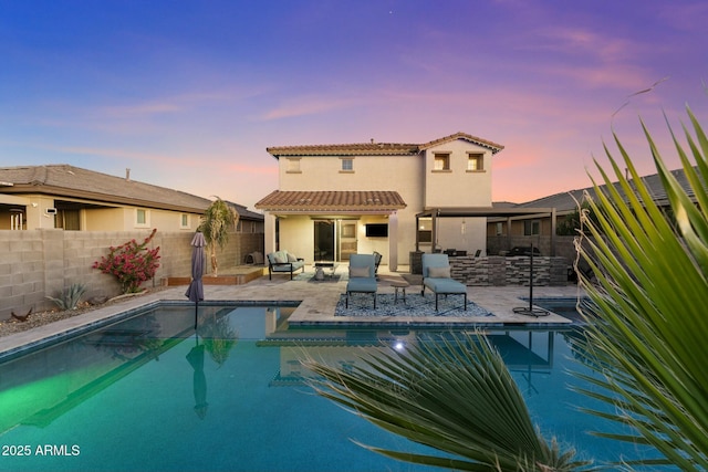 pool at dusk with a patio area and exterior kitchen