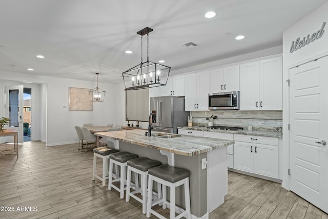 kitchen with a kitchen island with sink, white cabinets, light stone counters, and appliances with stainless steel finishes