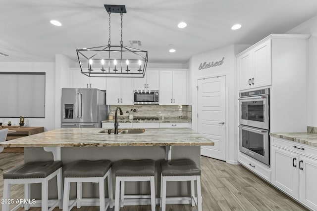 kitchen featuring light stone countertops, sink, an island with sink, white cabinets, and appliances with stainless steel finishes