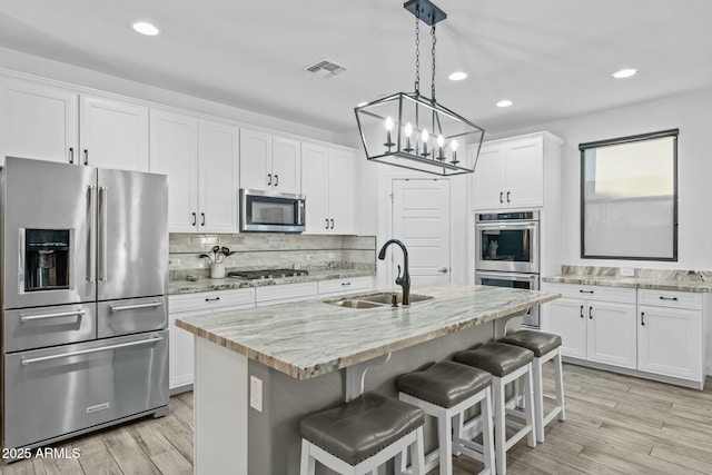 kitchen featuring light stone countertops, white cabinetry, a kitchen island with sink, and appliances with stainless steel finishes