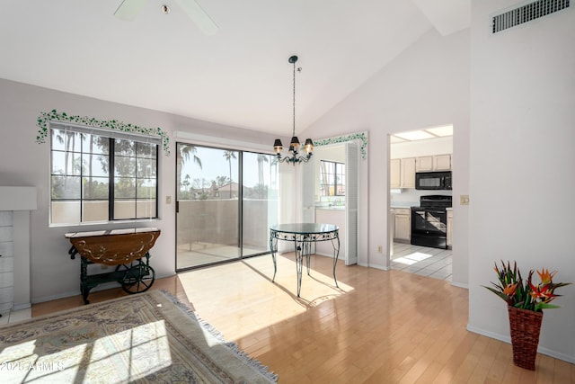 dining room featuring ceiling fan with notable chandelier, light hardwood / wood-style flooring, and high vaulted ceiling