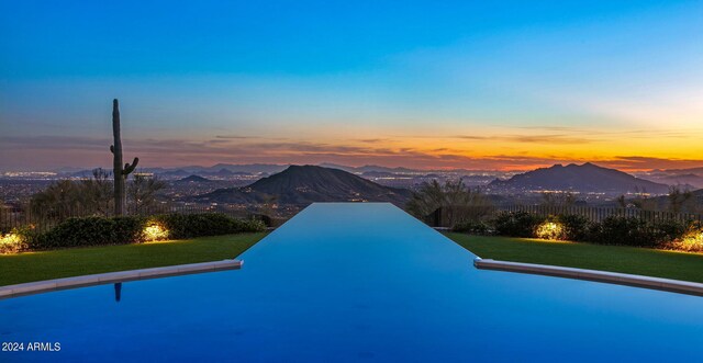 pool at dusk featuring a mountain view and a yard