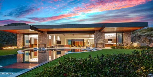 back house at dusk featuring a lawn and a patio