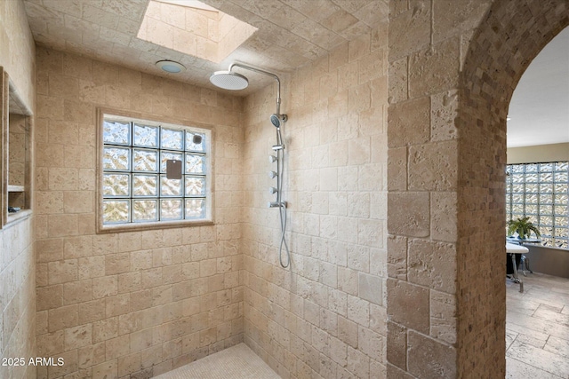 bathroom with a tile shower and a skylight