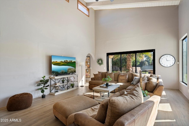 living room with beamed ceiling, light hardwood / wood-style flooring, and a high ceiling