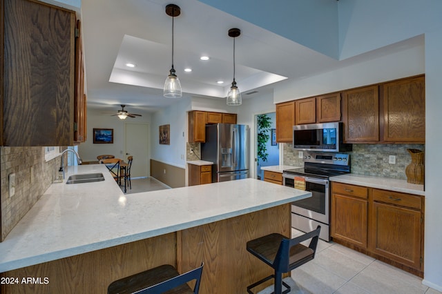 kitchen with sink, a kitchen breakfast bar, kitchen peninsula, a tray ceiling, and appliances with stainless steel finishes