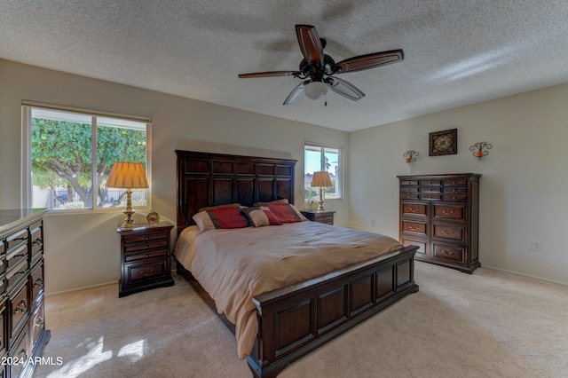 bedroom featuring ceiling fan, light colored carpet, a textured ceiling, and multiple windows