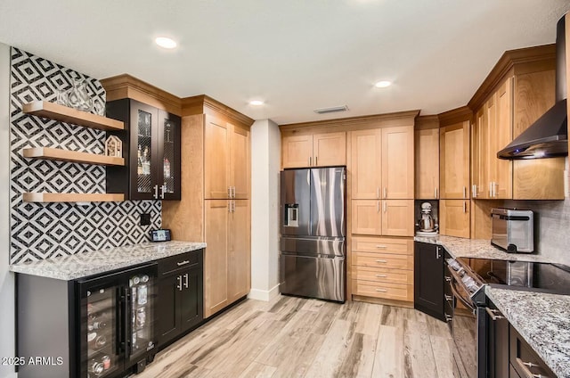 kitchen with wall chimney range hood, appliances with stainless steel finishes, wine cooler, and light stone counters