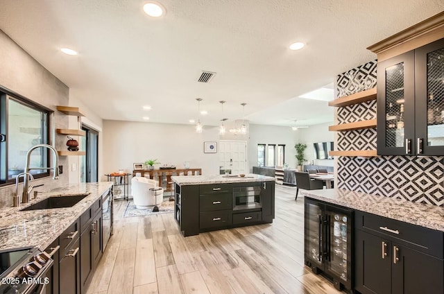 kitchen featuring decorative light fixtures, light stone counters, beverage cooler, and sink