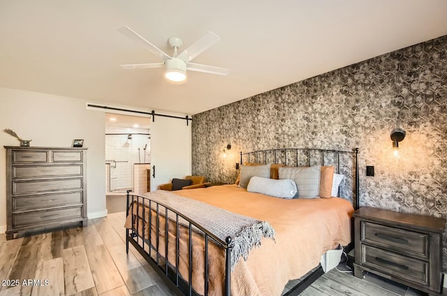 bedroom with a barn door, ceiling fan, and wood-type flooring