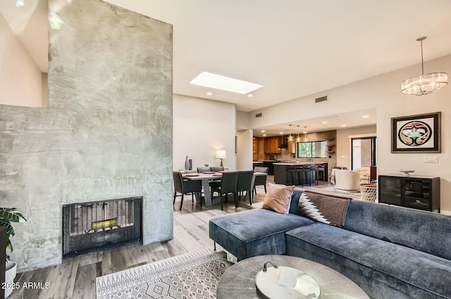 living room with a notable chandelier, a stone fireplace, light hardwood / wood-style flooring, and a skylight