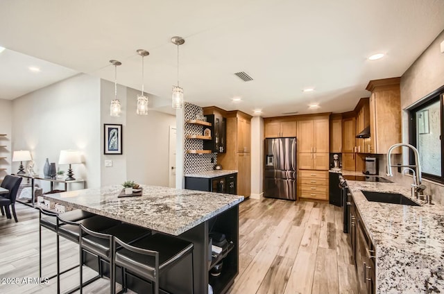 kitchen with stainless steel fridge with ice dispenser, light hardwood / wood-style flooring, light stone counters, backsplash, and a kitchen island