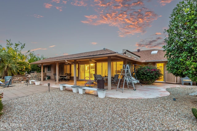 back house at dusk with ceiling fan and a patio area