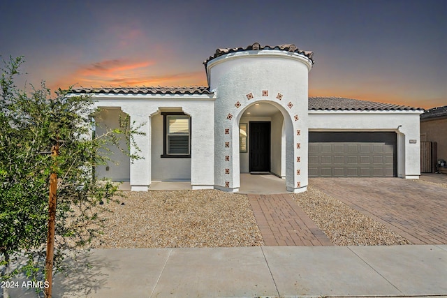 mediterranean / spanish home with a garage, a tiled roof, decorative driveway, and stucco siding