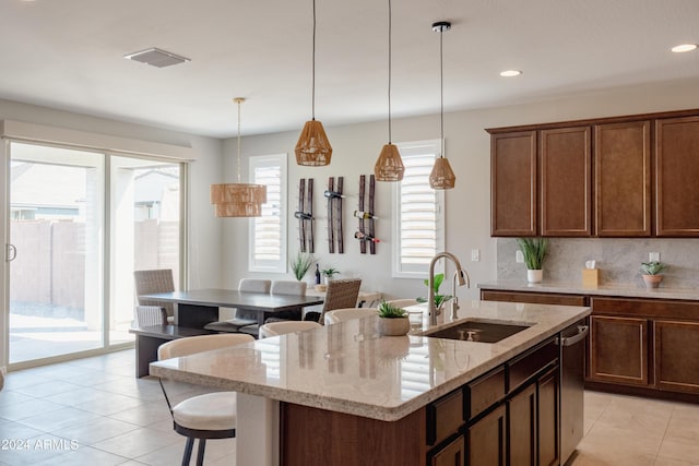 kitchen featuring decorative light fixtures, visible vents, decorative backsplash, a sink, and an island with sink