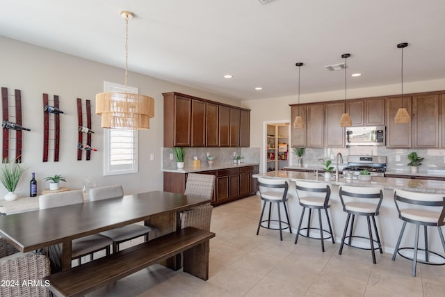 kitchen featuring decorative light fixtures, stainless steel appliances, a breakfast bar, visible vents, and a center island with sink