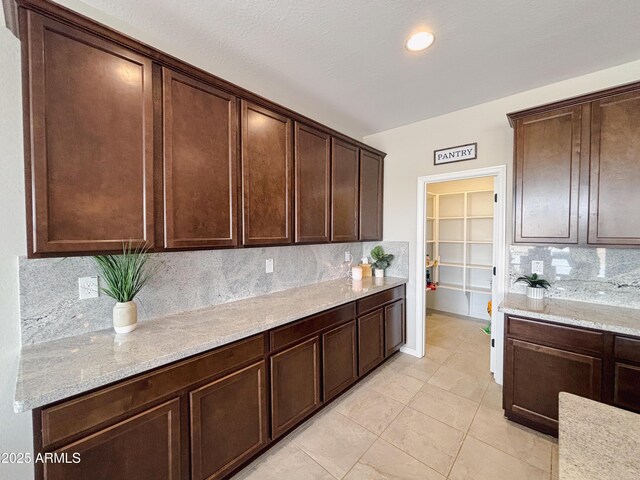 kitchen featuring tasteful backsplash, dark brown cabinetry, and light stone countertops