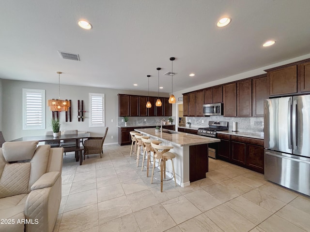 kitchen featuring stainless steel appliances, visible vents, open floor plan, a sink, and dark brown cabinetry