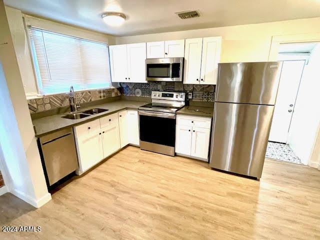 kitchen with white cabinets, light wood-type flooring, stainless steel appliances, and sink